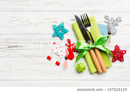 New year set of fork and knife on napkin. Top view of christmas decorations and reindeer on wooden background. Holiday family dinner concept with empty space for your design New year set of fork and knife on napkin. Top view of christmas decorations and reindeer on wooden background. Holiday family dinner concept with empty space for your design 107828129