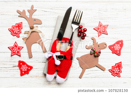 Top view of new year utensils on napkin with holiday decorations and reindeer on wooden background. Close up of christmas dinner concept Top view of new year utensils on napkin with holiday decorations and reindeer on wooden background. Close up of christmas dinner concept 107828130