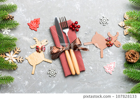 Top view of flatware tied up with ribbon on napkin on cement background. Close up of christmas decorations and reindeer. New Year holiday concept Top view of flatware tied up with ribbon on napkin on cement background. Close up of christmas decorations and reindeer. New Year holiday concept 107828133