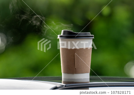coffee takeaway in a paper cup on top of the car roof green tree background at sunrise in the morning, selective focus, soft focus. coffee takeaway in a paper cup on top of the car roof green tree background at sunrise in the morning, selective focus, soft focus. 107828171