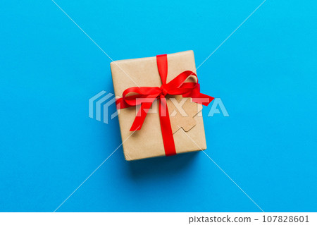 wrapped christmas or other holiday handmade present in paper with colored ribbon. Present box, decoration of gift on colourfull table, top view with copy space wrapped christmas or other holiday handmade present in paper with colored ribbon. Present box, decoration of gift on colourfull table, top view with copy space 107828601