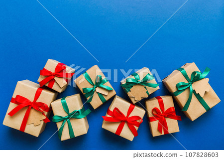 wrapped christmas or other holiday handmade present in paper with colored ribbon. Present box, decoration of gift on colourfull table, top view with copy space 107828603