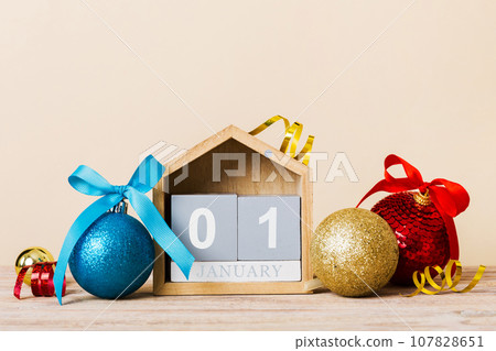 1 january. Christmas composition on colored background with a wooden calendar, with a gift box, toys, bauble copy space 107828651