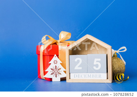 25 december. Christmas composition on colored background with a wooden calendar, with a gift box, toys, bauble copy space 25 december. Christmas composition on colored background with a wooden calendar, with a gift box, toys, bauble copy space 107828652