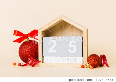 25 december. Christmas composition on colored background with a wooden calendar, with a gift box, toys, bauble copy space 25 december. Christmas composition on colored background with a wooden calendar, with a gift box, toys, bauble copy space 107828653