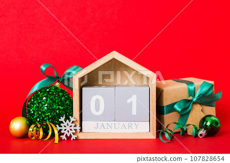 1 january. Christmas composition on colored background with a wooden calendar, with a gift box, toys, bauble copy space 1 january. Christmas composition on colored background with a wooden calendar, with a gift box, toys, bauble copy space 107828654