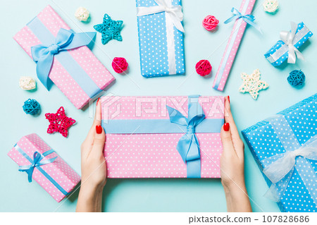 Top view of female hands holding a Christmas present on festive blue background. Holiday decorations. New Year holiday concept 107828686