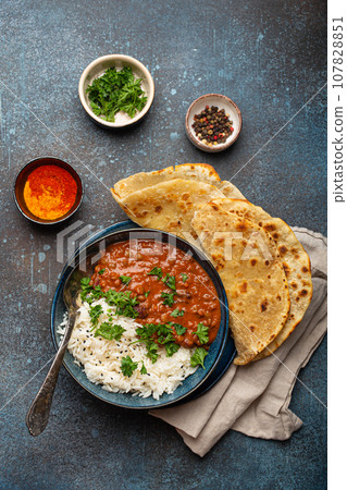 Traditional Indian Punjabi dish Dal makhani with lentils and beans in black bowl served with basmati rice, naan flat bread, fresh cilantro and spoon on blue concrete rustic table top view Traditional Indian Punjabi dish Dal makhani with lentils and beans in black bowl served with basmati rice, naan flat bread, fresh cilantro and spoon on blue concrete rustic table top view 107828851