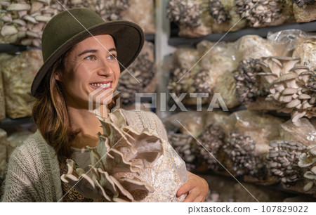 Young smiling woman holding grown medium with oyster mushrooms 107829022
