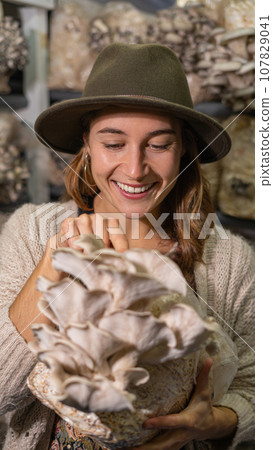 Young smiling woman holding grown medium with Organic oyster mushrooms 107829041