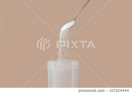 Spoon a handful of white collagen powder in a spoon over a glass. Spoon a handful of white collagen powder in a spoon over a glass. 107829444