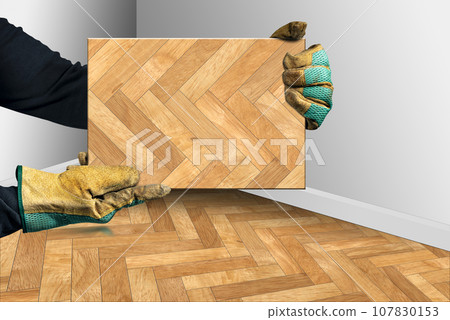 Gloved Hands Holding a Herringbone Wood Parquet Sample 107830153