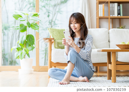年輕女子在客廳看智慧型手機 107830239