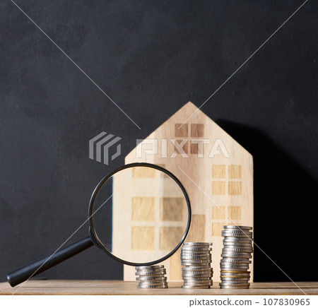 Wooden house, stack of coins, and a magnifying glass, representing the concept of real estate purchase, rental growth, and mortgage interest 107830965