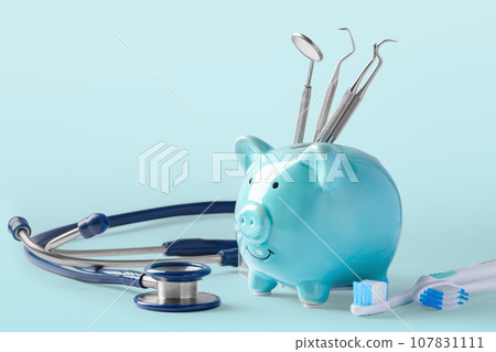Dental cost concept, piggy bank with dentist instruments on blue background, copy space Dental cost concept, piggy bank with dentist instruments on blue background, copy space 107831111