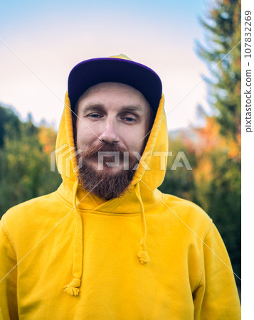 Red bearded millennial man with mustache in yellow hoody smiling portrait closeup Backpacker hiking climbing mountains 107832269