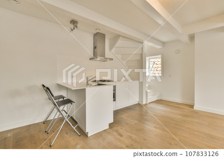 a kitchen and dining area in a room with white walls, hardwood flooring and an open door leading to the living room 107833126