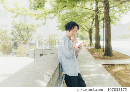 A man in his 30s using a smartphone on a city street 107833175
