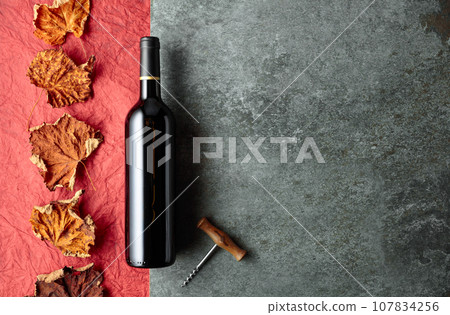Bottle of red wine with corkscrew and dried vine leaves. 107834256