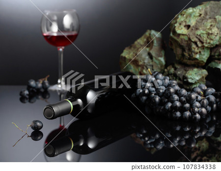 Blue grapes and red wine on a black reflective background. Blue grapes and red wine on a black reflective background. 107834338