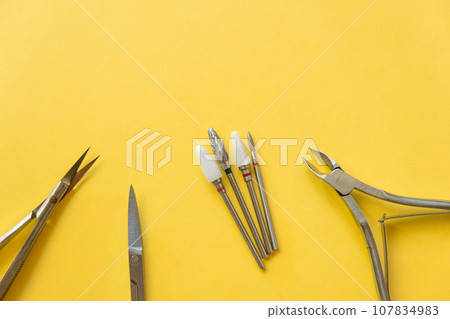 Professional manicure tools on yellow background. Manicure set. Top view. Cuticle pusher, cuticle trimmer and purpose scissor. Set of manicure and pedicure tools and cosmetics with space 107834983