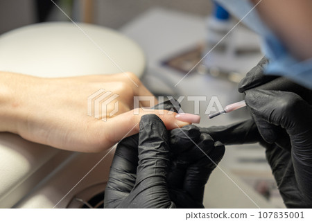 Female hands and tools for manicure, process of performing manicure in beauty salon. Nail care procedure in a beauty salon. Gloved hands of an experienced manicurist in gloves are varnished nails 107835001