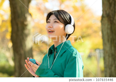 一個女人在陽光明媚的秋季公園享受音樂 一個女人在陽光明媚的秋季公園享受音樂 107835446