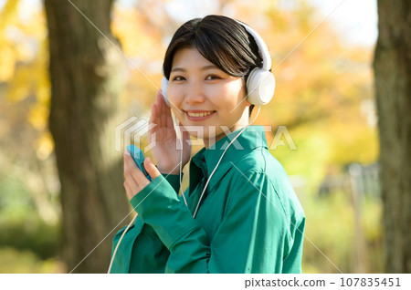 一個女人在陽光明媚的秋季公園享受音樂 一個女人在陽光明媚的秋季公園享受音樂 107835451