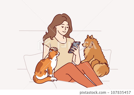 Woman owner of dog and cat sits on couch and plays on phone, enjoying spending time with pets 107835457