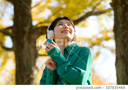 一個女人在陽光明媚的秋季公園享受音樂 一個女人在陽光明媚的秋季公園享受音樂 107835469
