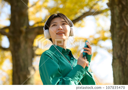 一個女人在陽光明媚的秋季公園享受音樂 一個女人在陽光明媚的秋季公園享受音樂 107835470