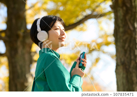 一個女人在陽光明媚的秋季公園享受音樂 一個女人在陽光明媚的秋季公園享受音樂 107835471