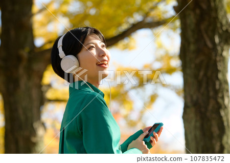 A woman enjoying music in a sunny autumn park A woman enjoying music in a sunny autumn park 107835472