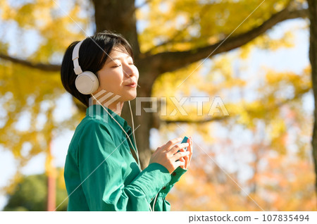 一個女人在陽光明媚的秋季公園享受音樂 一個女人在陽光明媚的秋季公園享受音樂 107835494