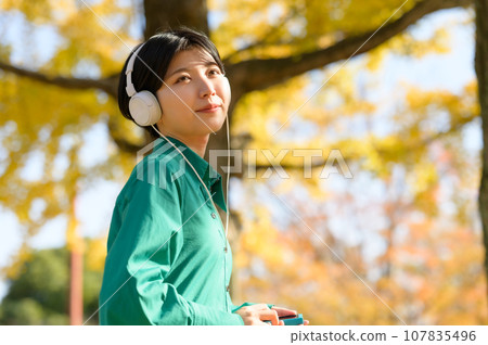 一個女人在陽光明媚的秋季公園享受音樂 一個女人在陽光明媚的秋季公園享受音樂 107835496