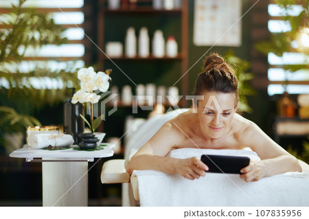 woman in spa salon using smartphone and laying on massage table 107835956