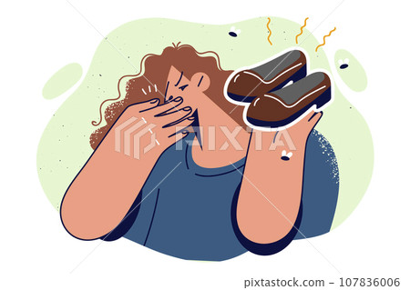 Woman holds smelly shoes and covers nose, disgusted by smell caused by sweating or skin fungus 107836006