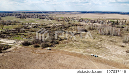 Agricultural machinery in a field near a small grove, aerial view. Agricultural land. Agricultural machinery in a field near a small grove, aerial view. Agricultural land. 107837446