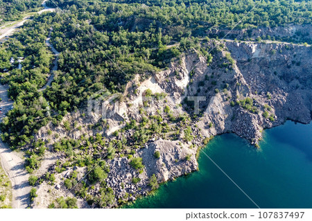 Rocky shore of the Radon Lake on a sunny summer morning. Aerial view of an old flooded granite quarry. A picturesque pond. 107837497