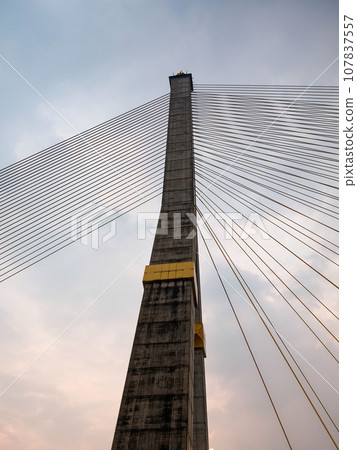 Set against the canvas of an overcast sky, a massive concrete pylon of a cable-stayed bridge stands tall, with cables forming a harp-like design. Set against the canvas of an overcast sky, a massive concrete pylon of a cable-stayed bridge stands tall, with cables forming a harp-like design. 107837557