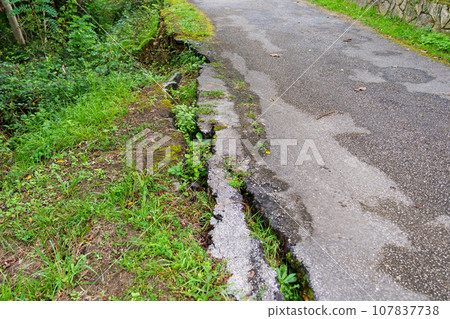 Collapsed broken asphalt road in the forest due to an earthquake. Crack close up Collapsed broken asphalt road in the forest due to an earthquake. Crack close up 107837738