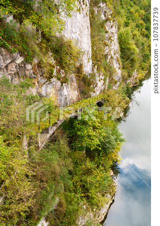 An ancient abandoned stone bridge on a wild rock with a forest. Sky reflection in river water An ancient abandoned stone bridge on a wild rock with a forest. Sky reflection in river water 107837739