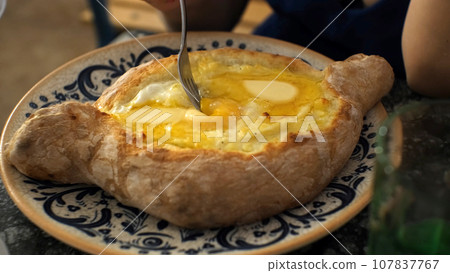 Close-up of hand of woman mixing suluguni cheese and egg yolk in Adjarian khachapuri, slow motion. Georgian traditional food concept 107837767