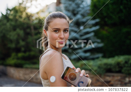Woman with diabetes connecting her smartphone to continuous glucose monitor sensor before exercising. Diabetic woman checking her blood sugar levels in real time before running. Woman with diabetes connecting her smartphone to continuous glucose monitor sensor before exercising. Diabetic woman checking her blood sugar levels in real time before running. 107837822