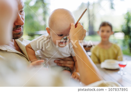 A small baby is being fed soup with big spoon. The mother feeding young child in a restaurant. A small baby is being fed soup with big spoon. The mother feeding young child in a restaurant. 107837891