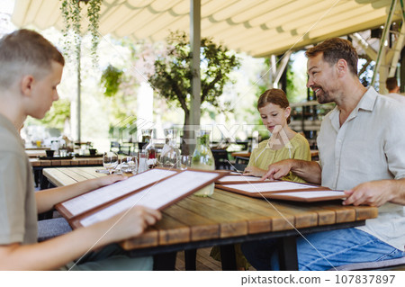 Father and children choosing food from menu. Single-parent family having dinner at restaurant. Concept of Father's Day. Father and children choosing food from menu. Single-parent family having dinner at restaurant. Concept of Father's Day. 107837897