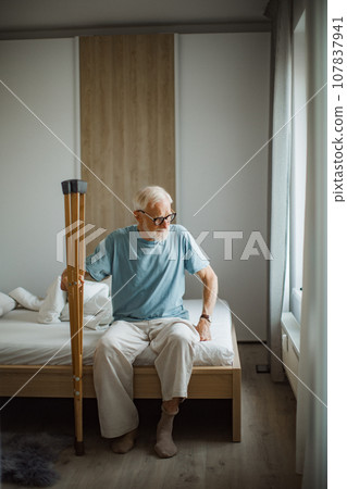 Elderly man with crutches trying to stand up from bed. Elderly man with crutches trying to stand up from bed. 107837941