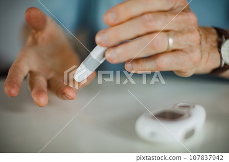 Diabetic senior man on wheelchair checking blood sugar level with fingerstick testing glucose meter. Elderly man with type 1 diabetes using blood glucose monitor at home. Diabetic senior man on wheelchair checking blood sugar level with fingerstick testing glucose meter. Elderly man with type 1 diabetes using blood glucose monitor at home. 107837942
