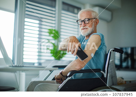 Diabetic senior man checking blood glucose level using continuous glucose monitor. Elderly man connecting CGM with smarphone to see blood sugar levels in real time. Diabetic senior man checking blood glucose level using continuous glucose monitor. Elderly man connecting CGM with smarphone to see blood sugar levels in real time. 107837945