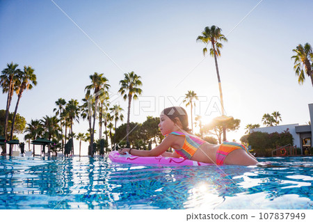 Girl floats on pink inflatable in the pool. Beach resort vacation by the sea. Winter and summer seaside resort holidays. Over-under underwater photography. Girl floats on pink inflatable in the pool. Beach resort vacation by the sea. Winter and summer seaside resort holidays. Over-under underwater photography. 107837949